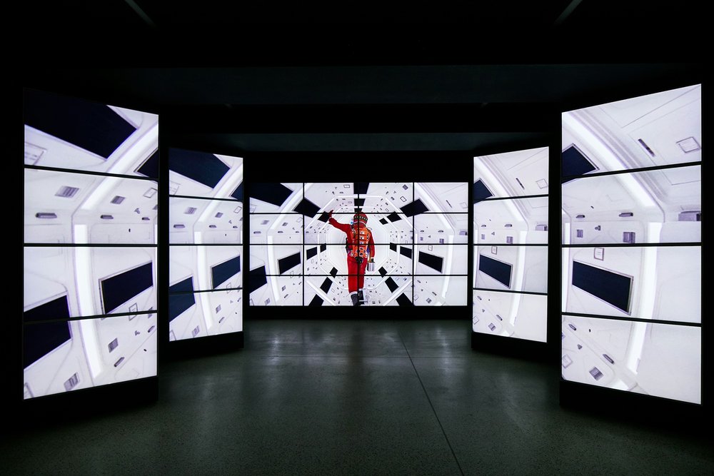 Image of screens showing the film 2001 – an astronaut in orange walks down an illuminated white tunnel
