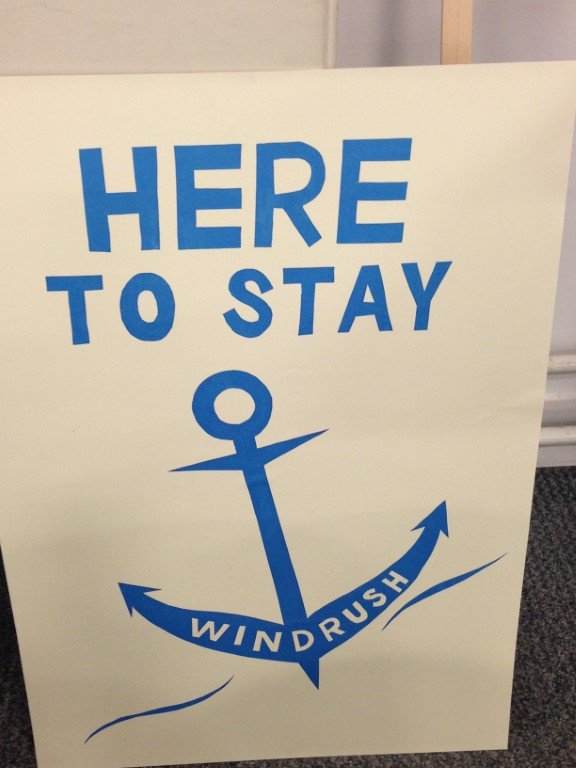 A white poster with a blue anchor and text reading "here to stay, windrush"