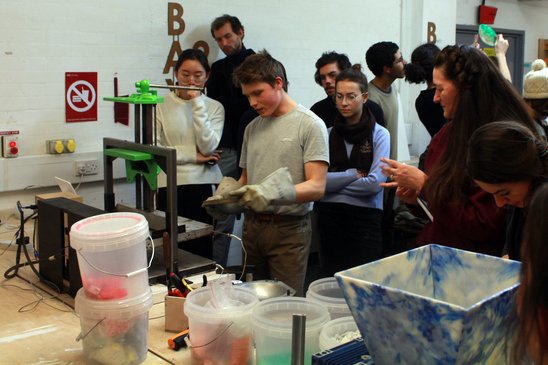A group of students gather around a table watching a plastic melting demonstration