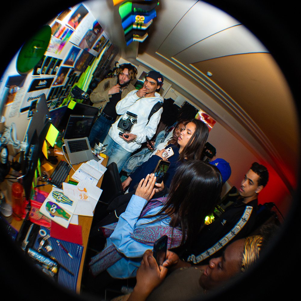 Room installation view using fish eye lens showing people gathered around a desk with screens.