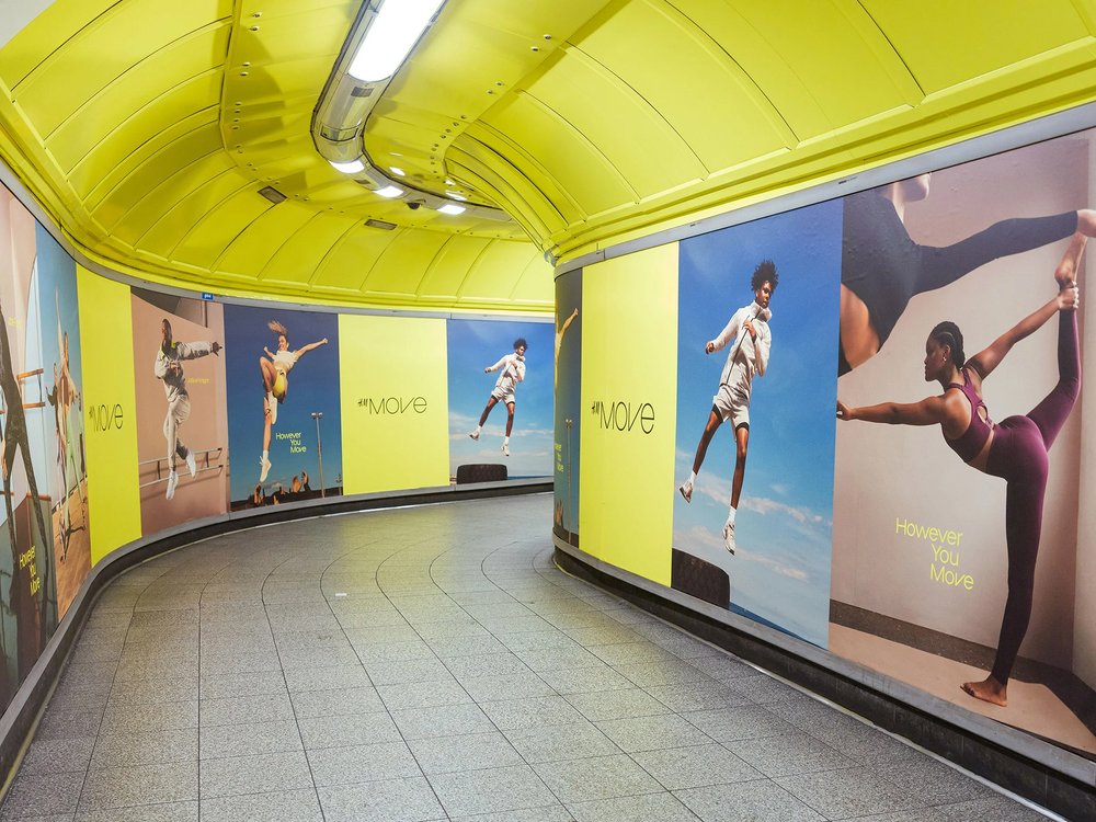 Photo of a curved pedestrian underpass (vivid yellow walls) with posters of athletes doing various sports