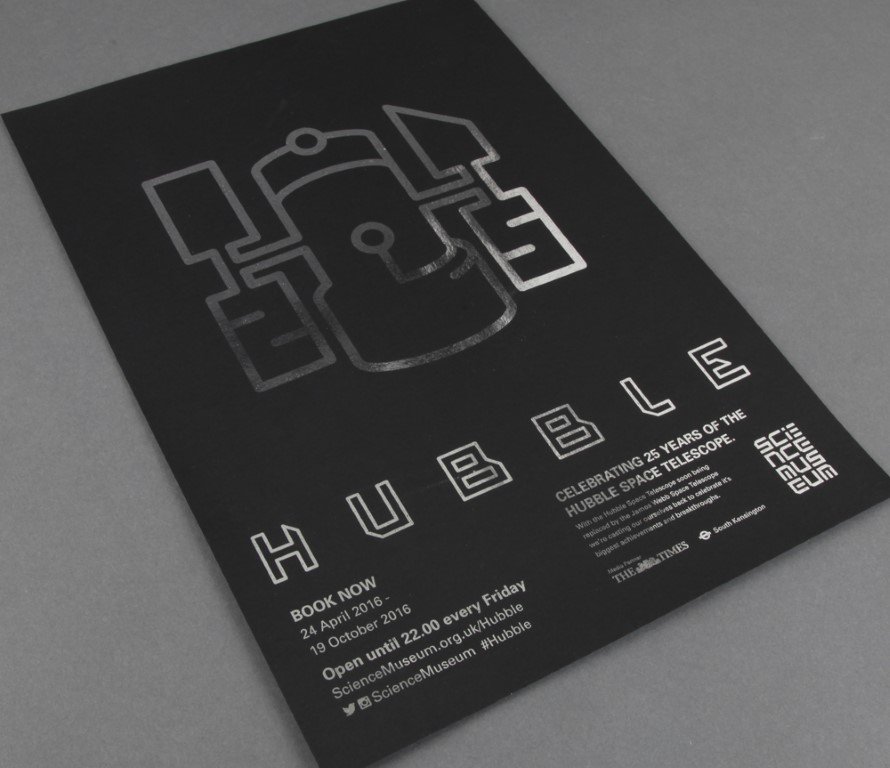 Silver printed text on black matte paper spelling out "hubble" with a graphic interpretation of the spacecraft